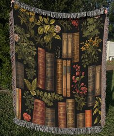 there is a blanket with books and flowers on it in front of some trees,