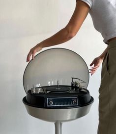 a woman standing next to a record player on top of a metal stand in front of a white wall