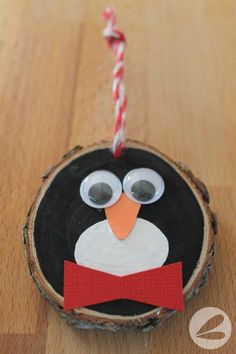 a penguin ornament hanging from a string on top of a wooden tree slice