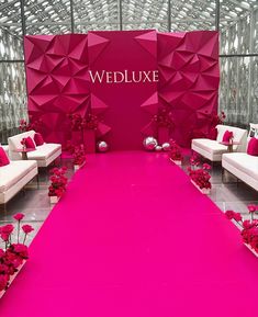 a pink wedding aisle with white couches and red flowers on the floor in front of it