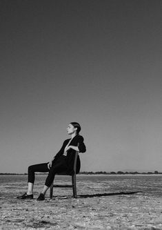 a woman sitting on top of a wooden bench in the middle of an empty field