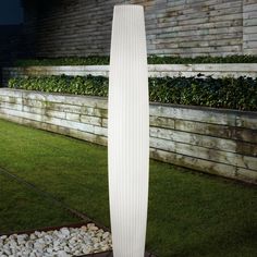 a tall white vase sitting on top of a wooden floor next to a lush green field