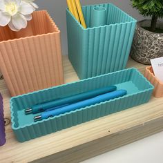 three different colored plastic containers with pens and pencils in them sitting on a table