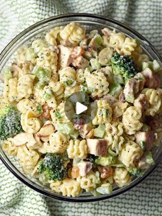 a glass bowl filled with pasta salad on top of a green and white table cloth