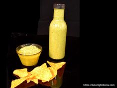 a glass bottle filled with yellow liquid next to some tortilla chips and salsa