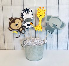 a bucket filled with lots of cupcake toppers next to a wall mounted giraffe, zebra and monkey