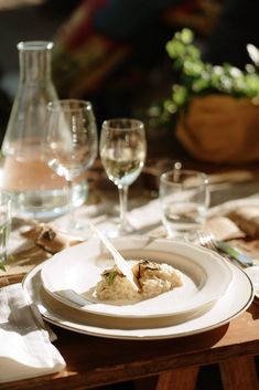 a white plate topped with food next to wine glasses and utensils on a table