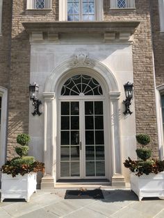 two white planters are in front of a large brick building with an arched glass door