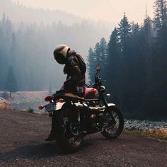 a person on a motorcycle in the middle of a road with trees and water behind them