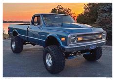 a large blue truck parked on top of a parking lot next to the ocean at sunset