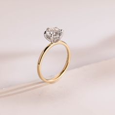 an engagement ring with a single diamond in the center on a white surface, close up