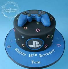 a blue and black birthday cake with two video game controllers on the top, happy 16th birthday tom