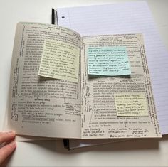 an open book with sticky notes attached to it and someone holding a pen in their hand