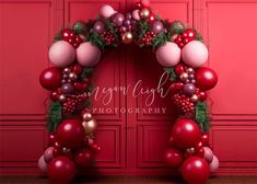 a red and pink christmas wreath with ornaments hanging from it's sides in front of a red wall