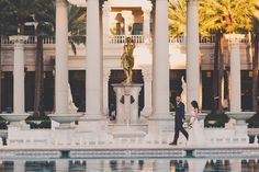 a bride and groom walking in front of a fountain