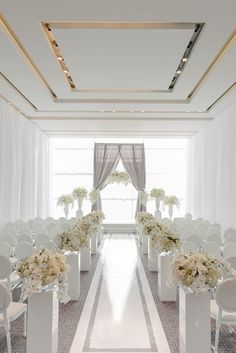 an aisle with white chairs and flowers in vases on either side is lined up against the wall