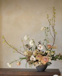 a vase filled with lots of flowers on top of a wooden table next to a wall