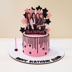 a pink birthday cake with black stars on it and two women sitting on top of the cake