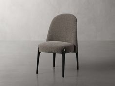 an upholstered chair with black legs and a grey backrest, in front of a white wall