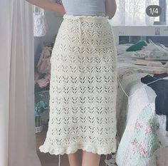 a woman standing in front of a bed wearing a white crochet skirt and grey tank top