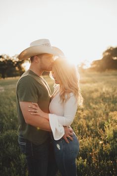 a man and woman standing together in a field at sunset with the sun behind them