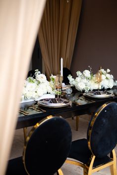 the table is set with black velvet chairs and white flowers in vases on it