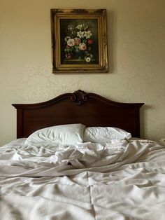 an unmade bed with white sheets and a painting on the wall