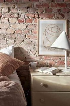 a brick wall in a bedroom next to a bed with pillows and a lamp on it