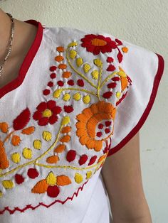 a woman wearing a white shirt with red, yellow and orange flowers embroidered on it