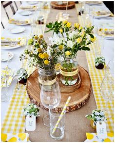 the table is set with yellow and white flowers in mason jar vases on wood slices