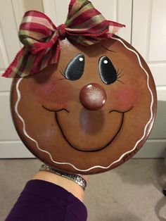 a hand holding up a wooden plate with a smiling face on it's face