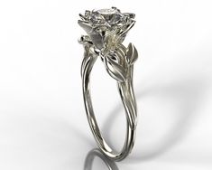 "A dainty 14k white gold ring showing a lotus set with a beautiful diamond or moissanite for your choice. The lotus is surrounded by a composition of leaves giving the ring a very natural look. ★See A Video Of This Amazing Ring Here★ https://youtu.be/WDBLPTtTrnQ Details: SKU: Fle39ww Gem Details: Center Gem: Choose between Moissanite or Natural diamond. Carat Weight: Choose from the \"Weight\" button Color/ Clarity: Moissanite - Forever One 'Charles & Colvard' arrive with the warranty certif Elegant Sterling Silver Flower Ring With Brilliant Cut, Elegant Diamond Solitaire Flower Ring, Elegant Silver Flower-shaped Diamond Ring, Elegant Silver Flower Diamond Ring, Elegant Solitaire Diamond Flower Ring, White Gold Solitaire Diamond Flower Ring, Elegant White Gold Solitaire Flower Ring, Delicate White Gold Diamond Flower Ring, Elegant Solitaire Flower Ring With Round Cut