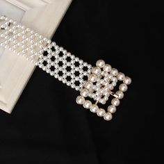 a white bracelet with pearls on it sitting in front of an open box and black background