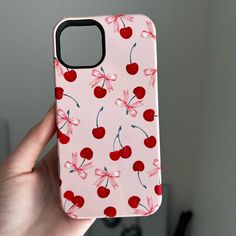 a hand holding up a pink case with cherries on it and red bowknots