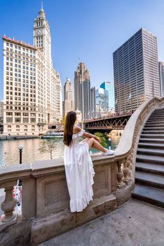 a woman is sitting on the edge of a bridge looking at the water and buildings