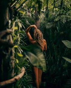 a woman standing in the middle of a jungle with her back to the camera and arms behind her head