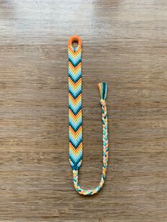 an orange, yellow and blue chevroned rope on a wooden surface with a hook