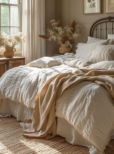 an unmade bed with white linens in a bedroom next to a window and potted plants