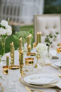 the table is set with white and gold plates, silverware, candles, and flowers