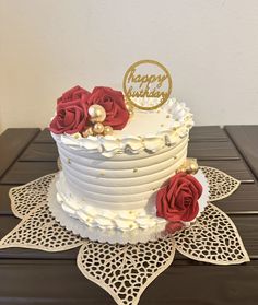 a white cake with red flowers and a happy birthday sign on top is sitting on a doily