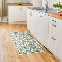 a kitchen with white cabinets and wooden floors has an area rug that looks like a flower pattern