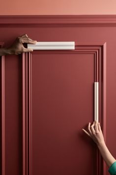 two hands are holding onto the door handle on a red door with pink walls and white trim