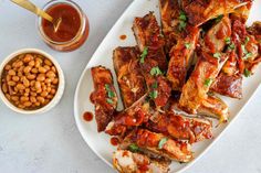 a white plate topped with ribs covered in sauce and beans next to a bowl of dipping sauce