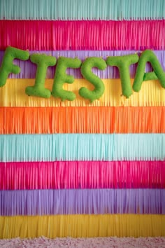 the word fiesta spelled out in neon colors on a colorful wall with streamers and fringes