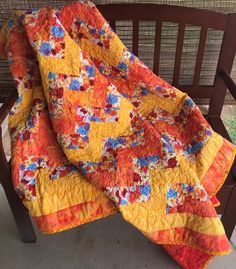 an orange and yellow quilt sitting on top of a wooden bench