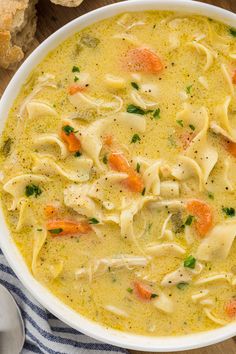 a bowl of chicken noodle soup on a wooden table with bread and spoons