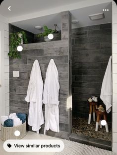 two white towels are hanging on the wall next to a gray tiled shower stall and stool