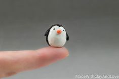 a tiny penguin figurine sitting on top of a persons finger in front of a gray background