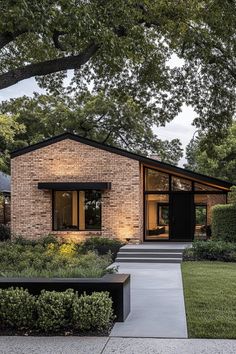 a brick house with steps leading up to the front door and side entrance, surrounded by greenery