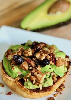 an avocado sandwich with nuts and raisins on it sits on a white plate